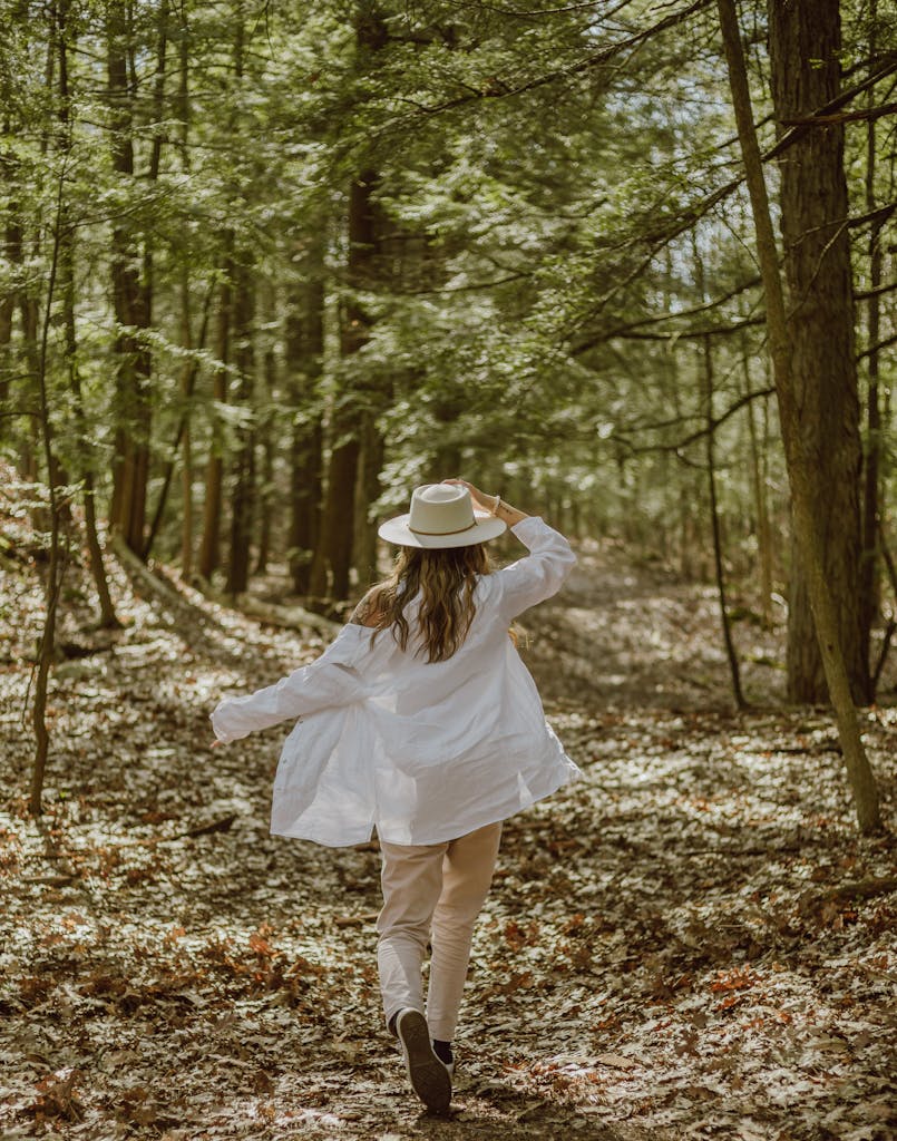 A woman in stylish attire walks along a serene forest path under the summer canopy.