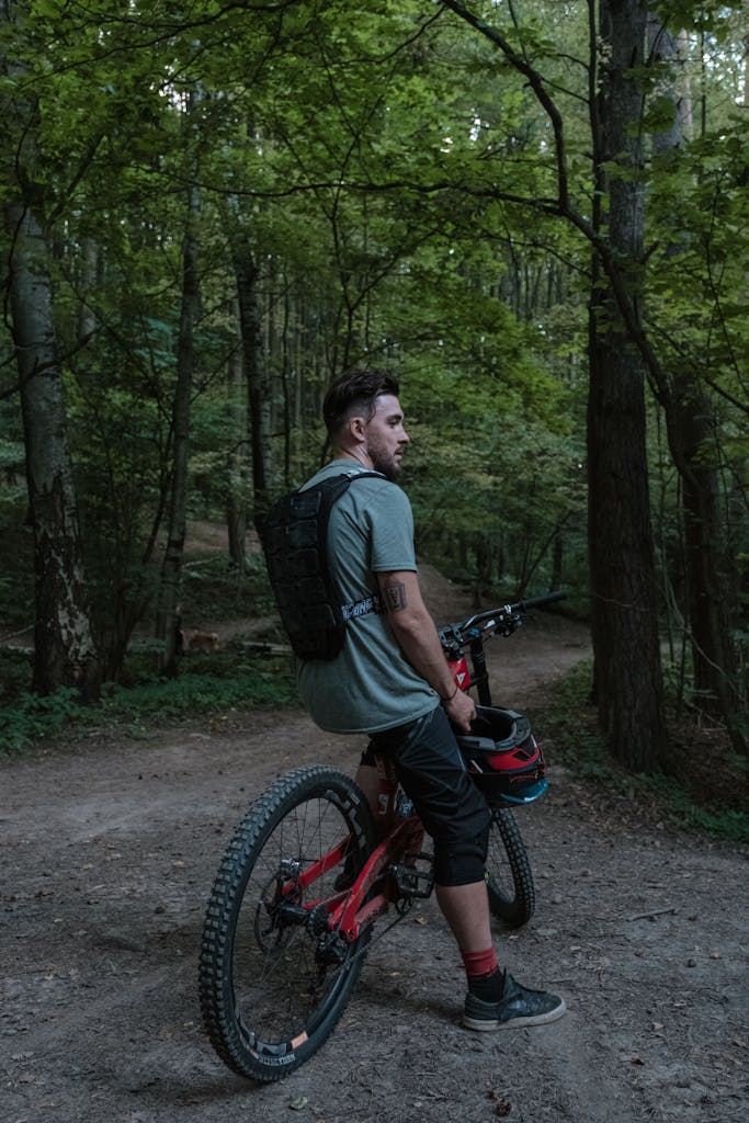 Man with mountain bike pausing on a forest trail amid lush greenery. Adventure awaits.